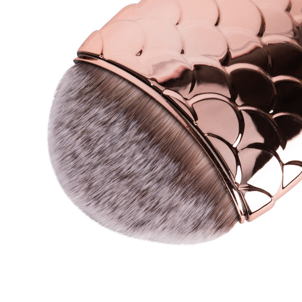 Lähikuva ruusukultaisesta kynsipölysiveltimestä, kompakti koko 8 × 5 cm, sopii kynsien puhdistukseen.

Mermaid Brush Rose Gold kynsipölysivellin käytössä manikyyrissä kynsipölyn poistamiseen kynsialueelta.